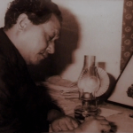 A vintage photograph of Kalaguru Bishnu Prasad Rabha, the Assamese cultural icon, writing at a desk with a kerosene lamp beside him, deep in thought.