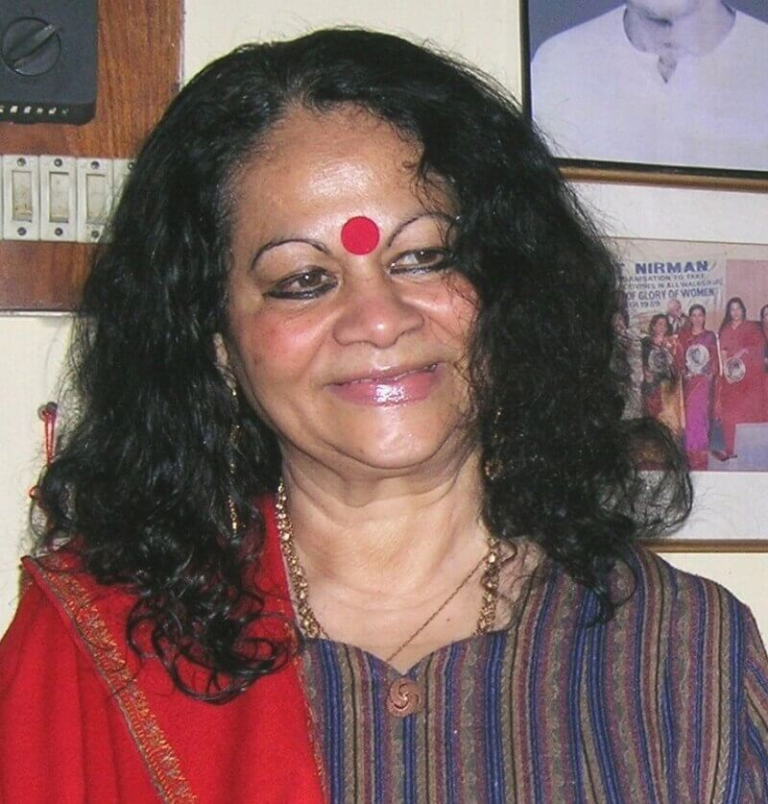 A photograph of Indira Goswami, the renowned Assamese writer and activist, wearing a red bindi and a traditional outfit, smiling warmly.
