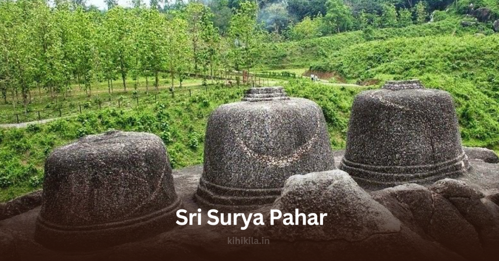 Ancient stone-carved Shiva Lingas at Sri Surya Pahar, an archaeological and religious site in Assam, surrounded by lush green hills.