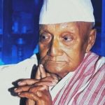 Portrait of Sonaram Chutia, an Assamese freedom fighter, scholar, and social reformer, wearing a traditional white cap and Assamese attire.