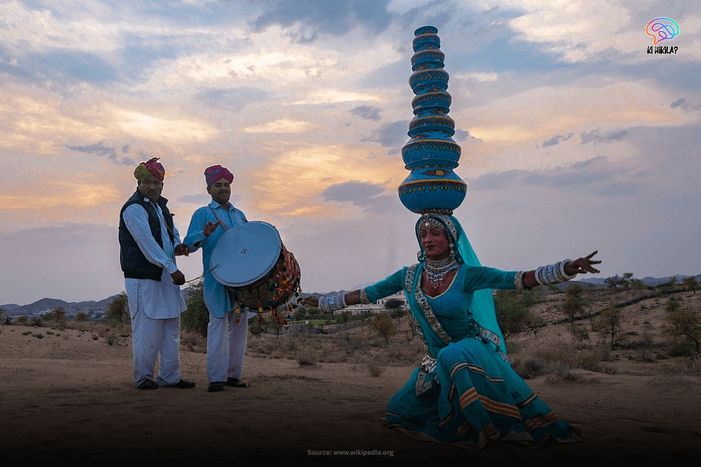 Rajasthan State Guide: Majestic Forts, Rich Heritage, and Key Facts for Students and Curious Minds A Kalbelia dancer in a vibrant blue costume with a stack of pots on her head, performing outdoors with two male musicians playing drums in Rajasthan.