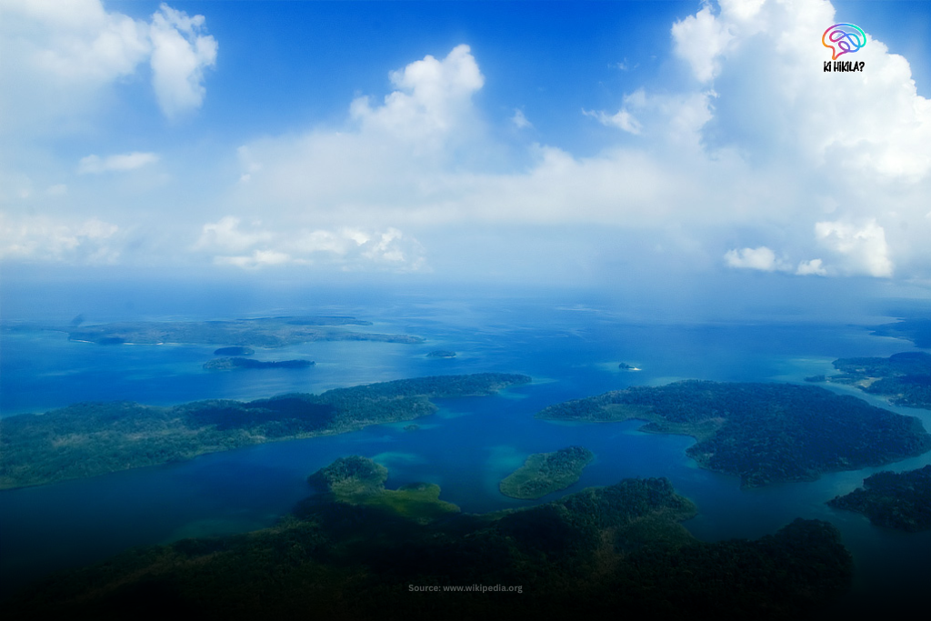 A breathtaking aerial view of the Andaman and Nicobar archipelago, showing dozens of green, forested islands scattered across the vast blue and turquoise sea.