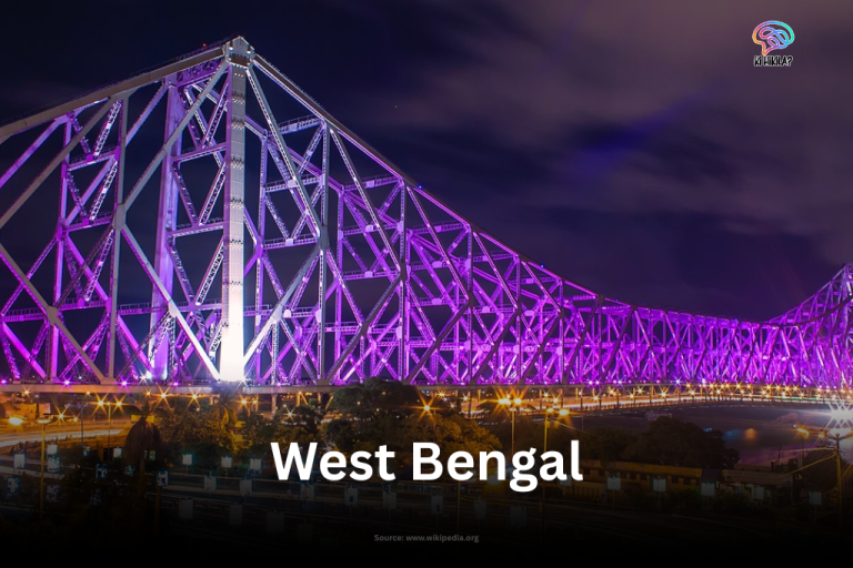 The iconic Howrah Bridge in Kolkata, West Bengal, brilliantly illuminated with purple lights against the dark night sky.