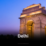 The illuminated arch of India Gate, a prominent war memorial in Delhi, standing against a deep blue twilight sky.