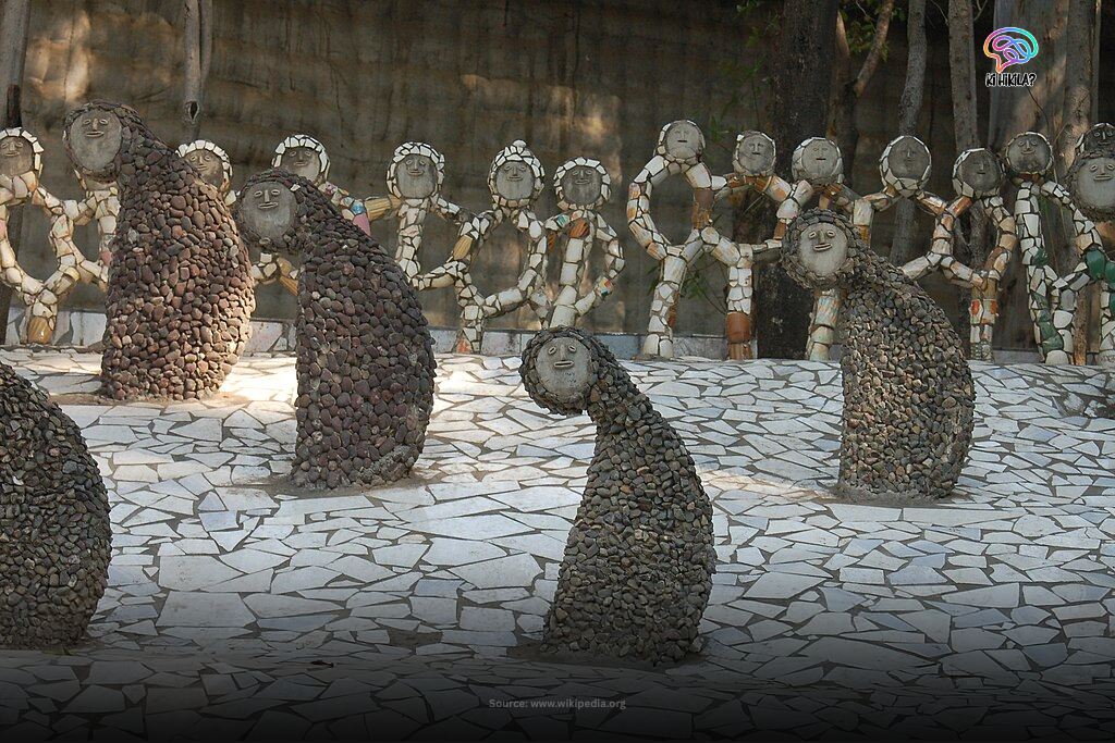 Sculptures of women in a courtyard at the Rock Garden in Chandigarh, made from recycled ceramic and tile pieces, with a waterfall in the background.
