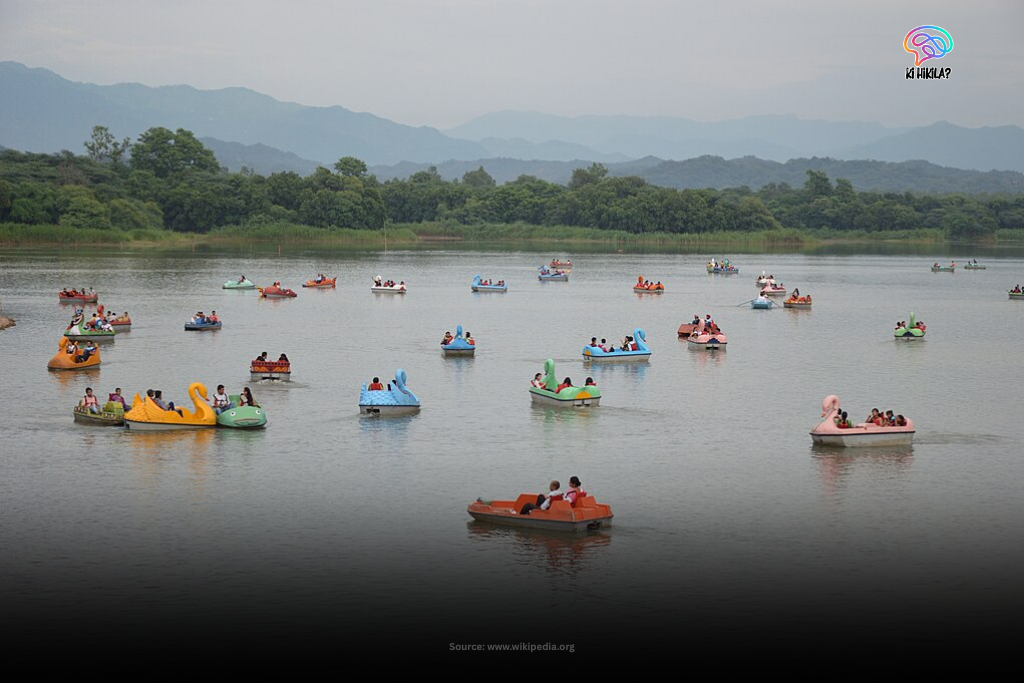 A serene view of Sukhna Lake in Chandigarh at what appears to be dusk or dawn, with the calm water reflecting the sky and distant hills.
