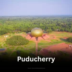 An aerial view of the Matrimandir in Auroville, Puducherry, surrounded by lush green landscapes.