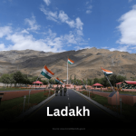 The Kargil War Memorial in Dras, Ladakh, with Indian flags lining the central walkway leading towards the rugged mountain backdrop.
