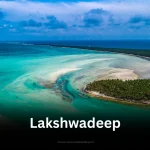 An aerial view of a pristine atoll in Lakshadweep, showcasing the turquoise lagoon, white sandbanks, and lush green coconut groves.