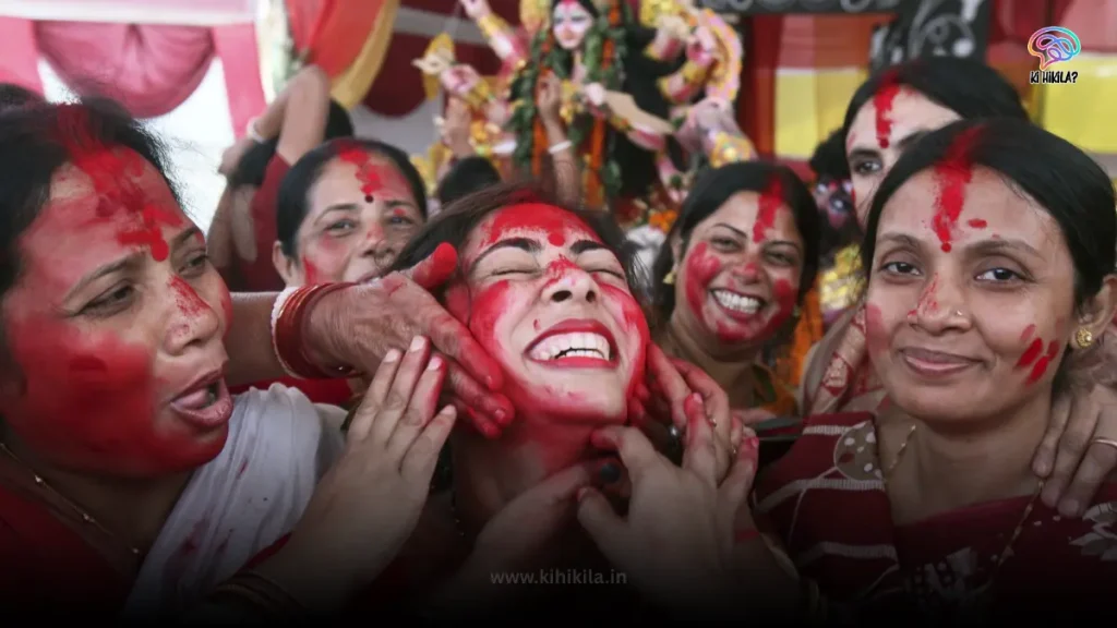 A close-up of several women celebrating the Sindoor Khela ritual during Durga Puja 2025, with their faces smeared with red vermilion.