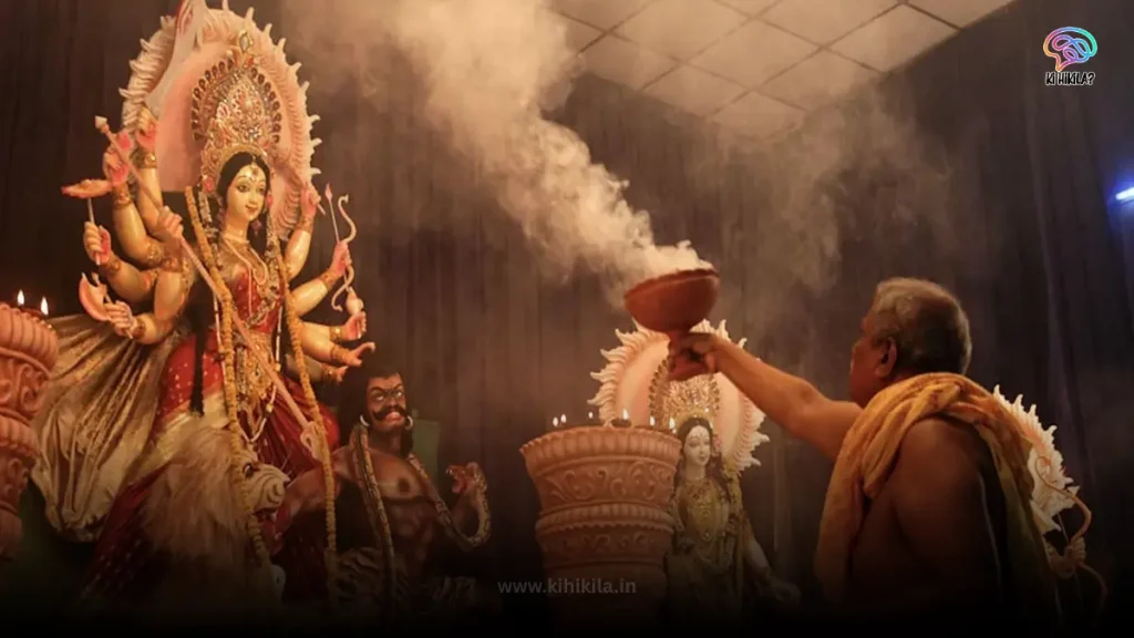 A priest performing a ritual with incense in front of a large, brightly lit Durga idol during Durga Puja 2025.