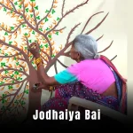 Jodhaiya Bai: A vibrant painting of a woman in a colorful Rajasthani lehenga, playing a traditional instrument with a desert backdrop.
