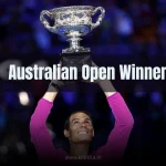 Ultimate List of Australian Open Winners: A jubilant tennis player in a pink shirt raising a silver trophy with both hands, smiling against a blurred blue-lit crowd background.